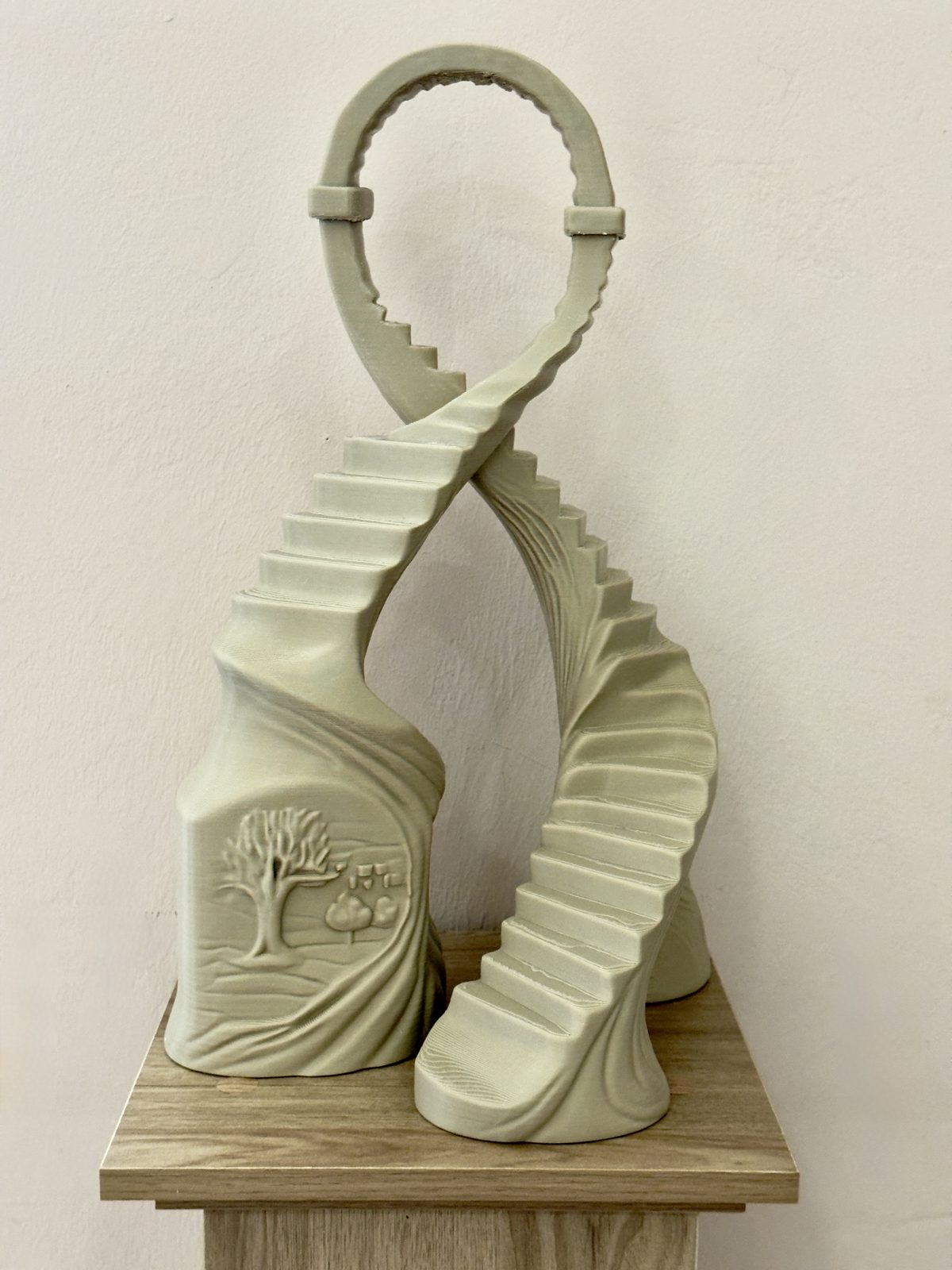 Soglia dell'Altrove — alberi che diventano scale e si incontrano in un arco a forma di 8, scultura color pietra su piedistallo